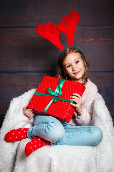 Feliz niña sonriente con cajas de regalo de Navidad.. concepto de Navidad. Sonriente niño divertido en cuernos de ciervo sobre fondo de madera —  Fotos de Stock