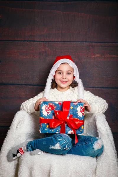Feliz niña sonriente con regalo de Navidad box.Christmas concepto. Sonriente chica bastante divertida en Santa sombrero sobre fondo de madera . —  Fotos de Stock