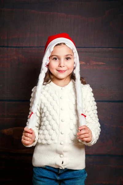 Счастливая маленькая улыбающаяся девочка. Смешная девушка в шляпе Санты на деревянном фоне . — стоковое фото