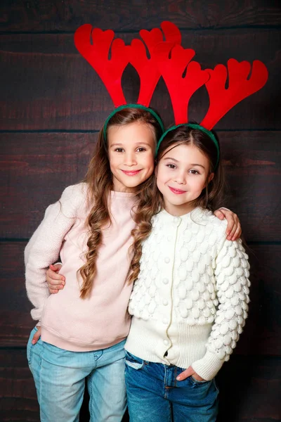 Две счастливые маленькие улыбающиеся девочки. Рождественская концепция. Улыбающиеся смешные сестры в оленьих рогах в студии . — стоковое фото