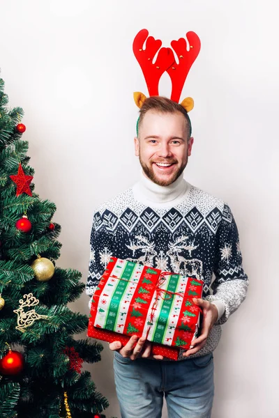 Homem de camisola segurando presentes perto da árvore de Natal — Fotografia de Stock