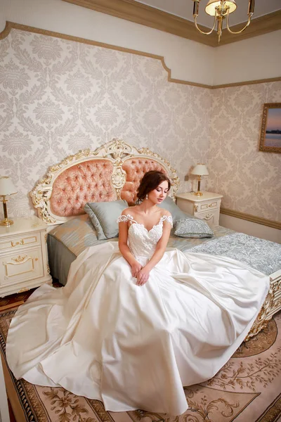 Casamento. Noiva em belo vestido sentado no sofá no interior do estúdio branco como em casa. Estilo de casamento na moda tiro em comprimento total . — Fotografia de Stock