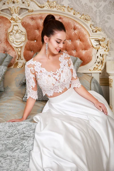 Svatba. Nevěsta v krásných šatech sedí na pohovce v bílých studio interiér jako doma. Módní svatební styl — Stock fotografie