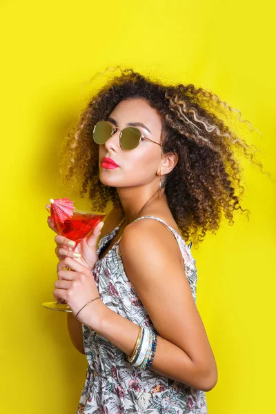 Beauty portrait of young african american girl with afro hairstyle in sunglasses. Girl posing on yellow background, looking at camera. Studio shot. — Stock Photo, Image