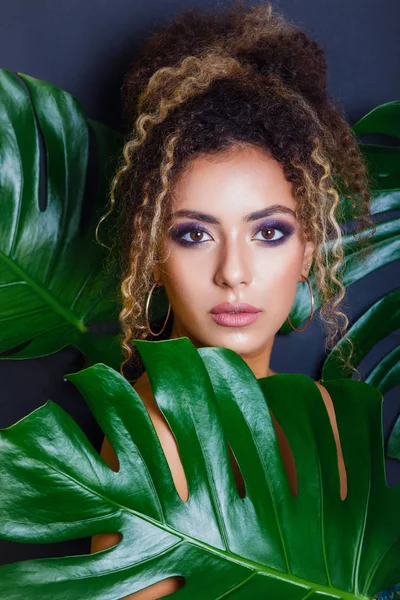 Close-up Retrato de uma mulher negra afro-americana com maquiagem noturna e folhas tropicais sobre fundo preto — Fotografia de Stock