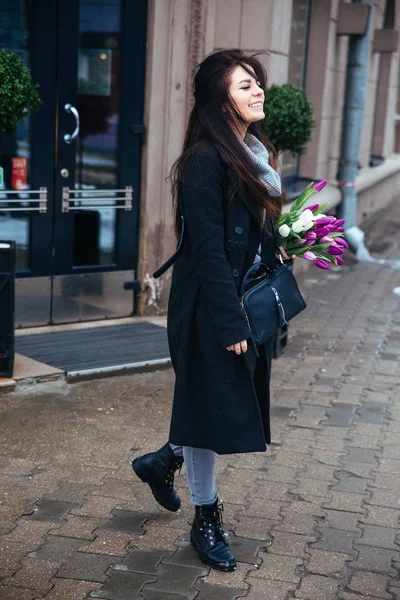 Chica joven caminando en una vieja calle de la ciudad europea con un ramo de lirios en la mano — Foto de Stock