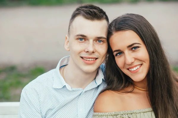 Gelukkige jonge paar verliefd op een bankje zitten en knuffelen — Stockfoto