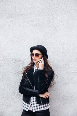 Gülümseyen kentsel kız akıllı telefon Yüzünde gülümsemeyle kullanır. Moda kız açık havada eğleniyor bir rock siyah stil giyen portresi