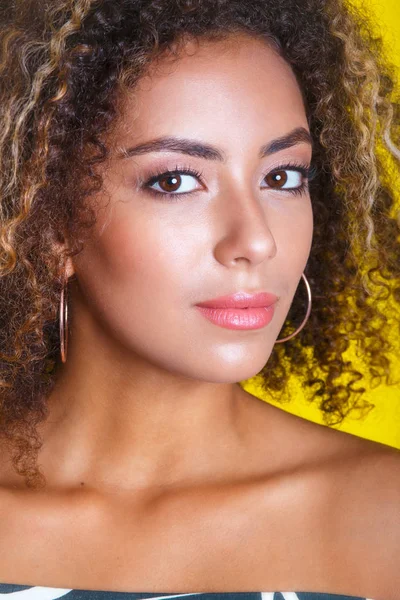 Retrato de belleza de una joven afroamericana con peinado afro. Chica posando sobre fondo amarillo, mirando a la cámara . — Foto de Stock