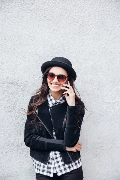 Gülümseyen kentsel kız akıllı telefon Yüzünde gülümsemeyle kullanır. Moda kız açık havada eğleniyor bir rock siyah stil giyen portresi — Stok fotoğraf