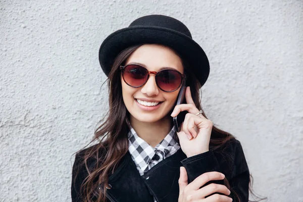 Χαμογελαστό κορίτσι αστικές χρήσεις έξυπνο τηλέφωνο με χαμόγελο στο πρόσωπό της. Πορτρέτο της μόδας Γκιρ φορώντας μαύρο ροκ ύφος διασκεδάζοντας σε εξωτερικούς χώρους — Φωτογραφία Αρχείου