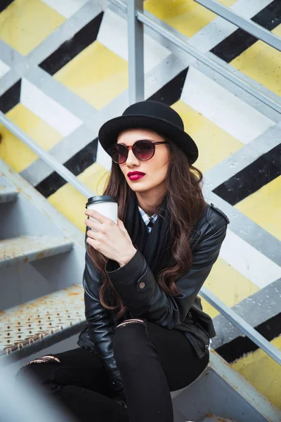 Young stylish woman in a city street sitting and drinking coffee or tea . — Stock Photo, Image