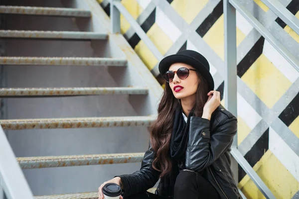 Young stylish woman in a city street sitting and drinking coffee or tea . — Stock Photo, Image
