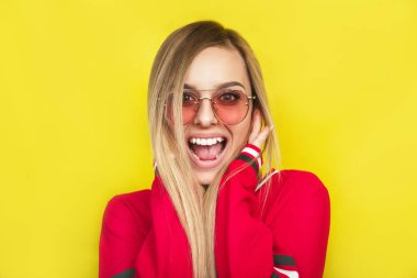 Güneş gözlüklü genç ve güzel kadın sarı arka plan üzerinde şaşırttı