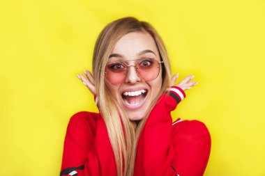 Güneş gözlüklü genç ve güzel kadın sarı arka plan üzerinde şaşırttı