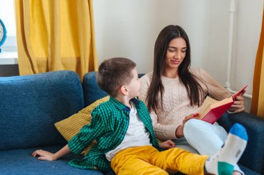 Anne ve küçük oğlu evde birlikte vakit geçirirken kitap okuyup gülümsüyorlar.
