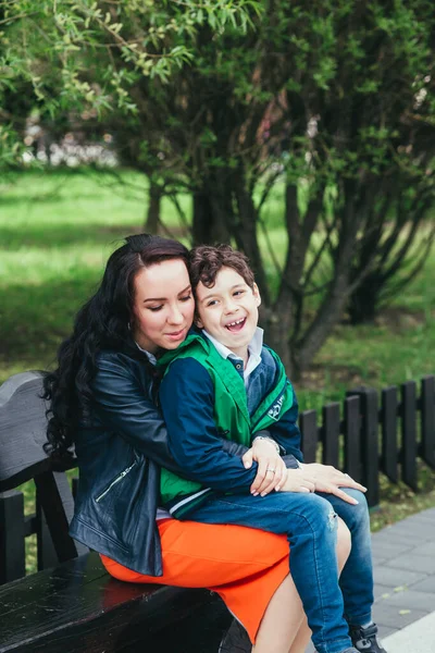 Söt liten pojke sitter i sin mors knä i parken. En moders kärlek och ömhet — Stockfoto