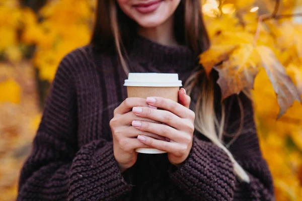 Taza de café de papel en las manos de las mujeres en el fondo de otoño — Foto de Stock