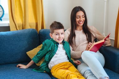 Güzel Hintli kadın kanepede oturuyor ve sevimli oğluna kitap okuyor.