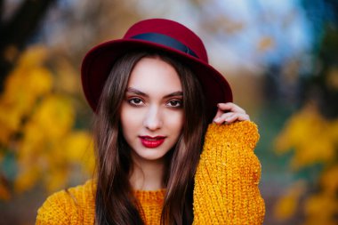 Parlak sarı kazaklı, kırmızı dudaklı güzel bir kadının portresi güneşli bir sonbahar gününün tadını çıkarıyor.