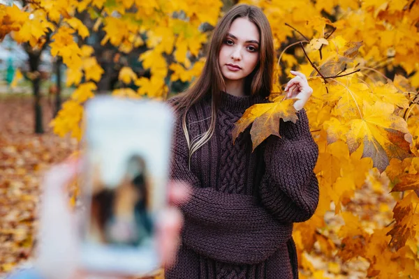 Beautiful young woman posing while her boyfriend is taking a photo in autumn park — Stock Photo, Image