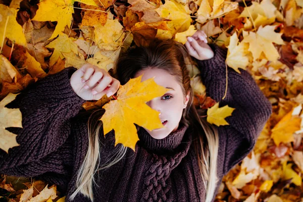 Beautiful young woman with autumn maple leaves lying on ground — Stock Photo, Image