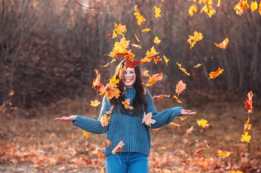 Young woman in autumn park playing with foliage.