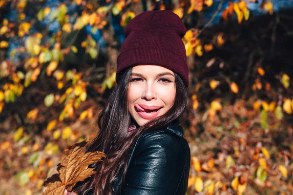 Stylish young woman in a hat and a plaid shirt in autumn park on a sunny day — Stock Photo, Image