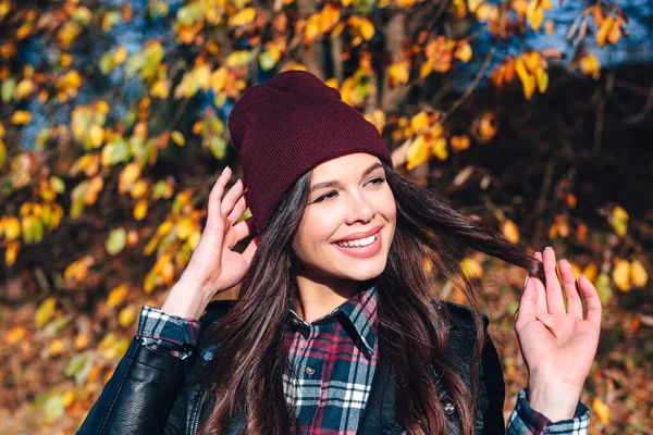 Stylish young woman in a hat and a plaid shirt in autumn park on a sunny day — Stock Photo, Image