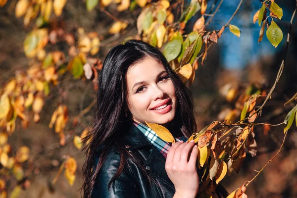 Mujer feliz bastante joven en ropa elegante con una hermosa sonrisa sostiene en su mano una hoja amarilla de otoño — Foto de Stock