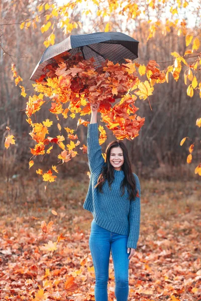 Girl makes rain from the leaves in autumn park