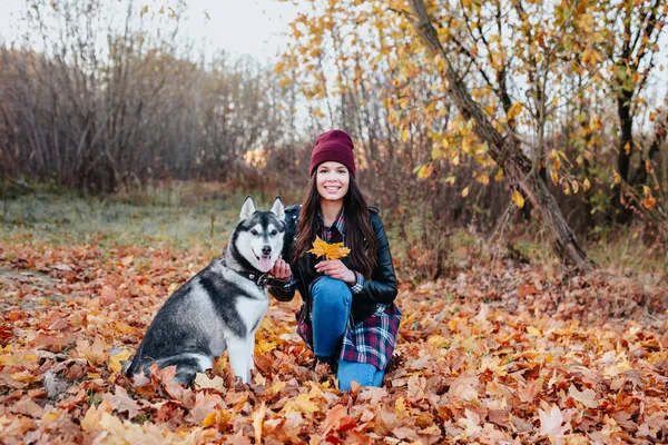 Χαμογελώντας κομψή γυναίκα περπατώντας με husky της το φθινόπωρο ημέρα. — Φωτογραφία Αρχείου