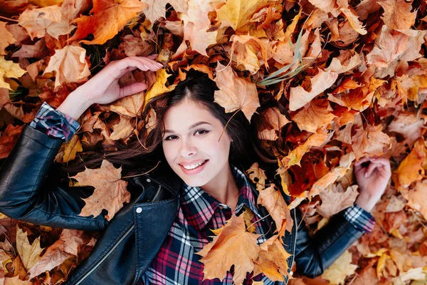 Carefree woman relaxing and lying on autumn leaves in park — Stock Photo, Image