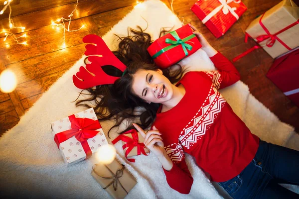 Hermosa mujer divertida con luces de Navidad y regalos tumbados en el suelo. Feliz Navidad y Feliz Año Nuevo — Foto de Stock