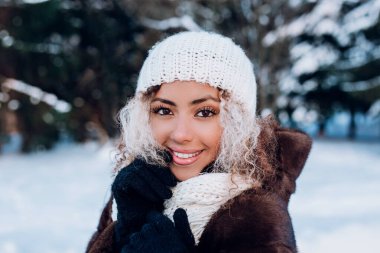 Gülümseyen genç bir kadın yüzüne dokunuyor, şık beyaz örgü örüyor kış şapkası ve eldiven takıyor..