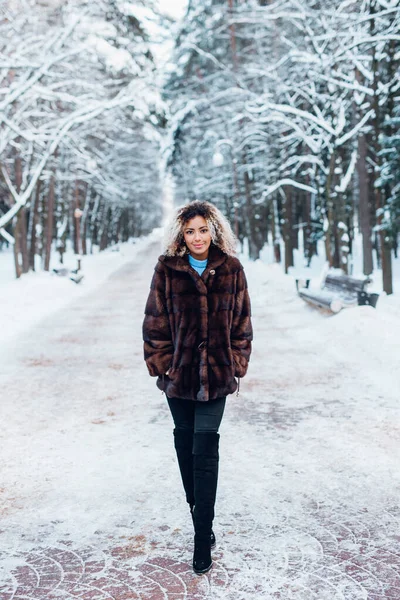 겨울 공원에서 모피 코트를 입고 걷고 있는아 프로 미국인 소녀의 전신 사진 — 스톡 사진