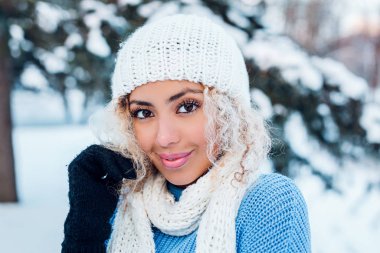 Gülümseyen genç kadın yüzüne dokunuyor ve kış parkında kameraya bakıyor..