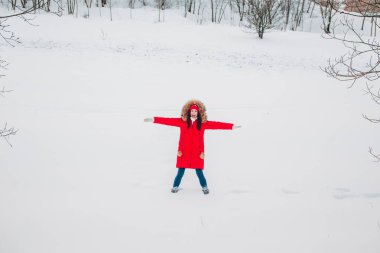 Kırmızı elbiseli genç kadın kış parkında karla oynuyor.