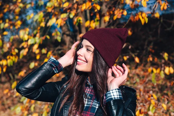 Stylish young woman in a hat and a plaid shirt in autumn park on a sunny day — Stock Photo, Image