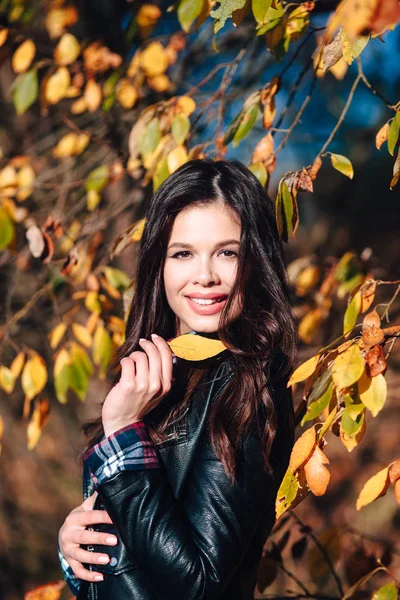 Mooie jonge gelukkige vrouw in stijlvolle kleren met een mooie glimlach houdt in haar hand een herfst geel blad — Stockfoto