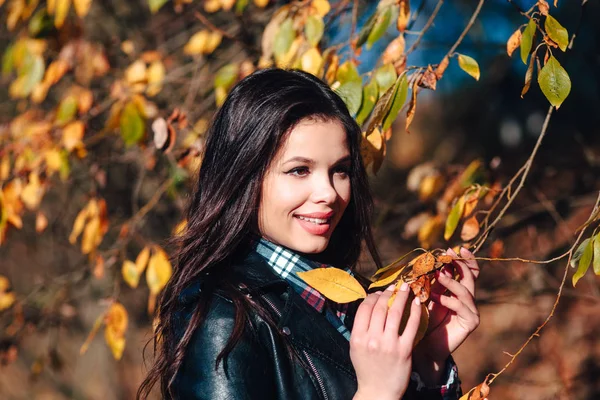 Ładna młoda szczęśliwa kobieta w stylowych ubraniach z pięknym uśmiechem trzyma w ręku jesienny żółty liść — Zdjęcie stockowe