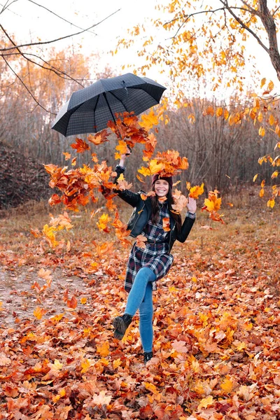 Smiling girl with umbrella throwing leaves in the air — Stock Photo, Image