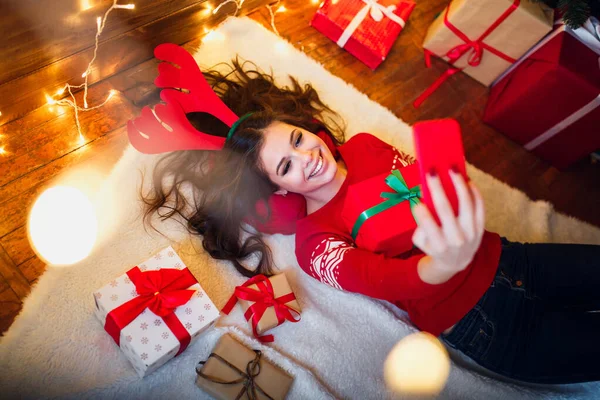 Улыбающаяся девушка делает селфи со смартфоном и лежит на полу. Рождественское настроение — стоковое фото
