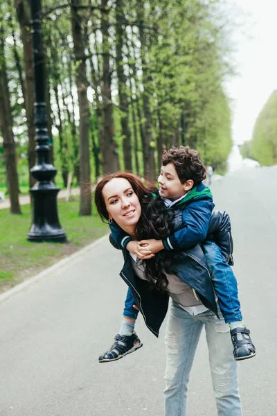 Joven madre piggyback su pequeño hijo fuera — Foto de Stock