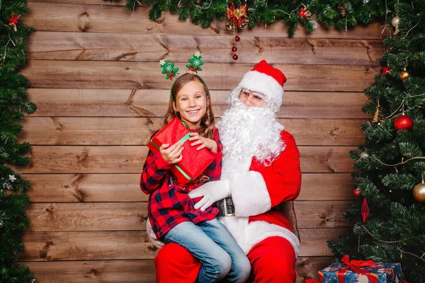 Santa Claus sitting with a little cute girl over Christmas background. — Stock Photo, Image