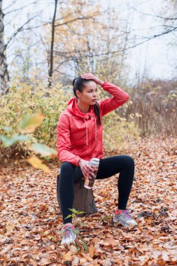 Genç koşucu ahşap kütükte oturuyor ve içme suyu içiyor.