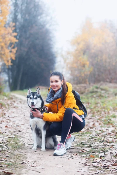 Porträtt av ung kvinna kramar sin husky hund i höstparken — Stockfoto