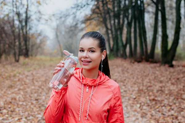 Junge schöne Frau trinkt Wasser beim morgendlichen Joggen im Herbstpark — Stockfoto