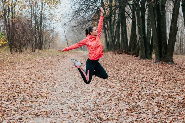 年轻快乐的女人在秋天的公园里跳跃。 在一个温暖的秋日，健身女孩在外面训练 — 图库照片