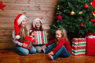 Noel Baba şapkalı, Noel ağacının yanında hediyeleri olan üç komik kız kardeş.